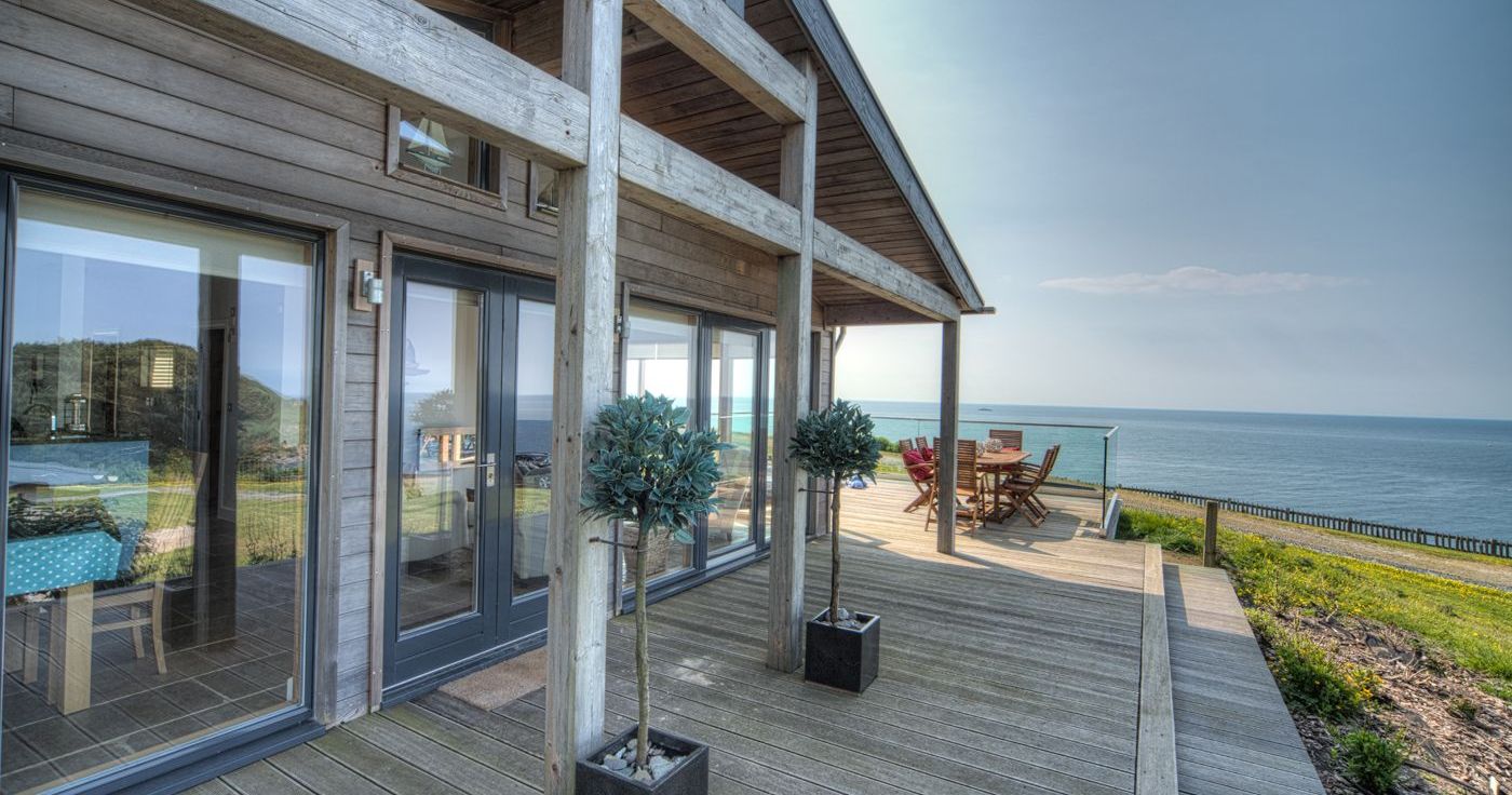 Modern wooden house with a large deck overlooking the ocean.