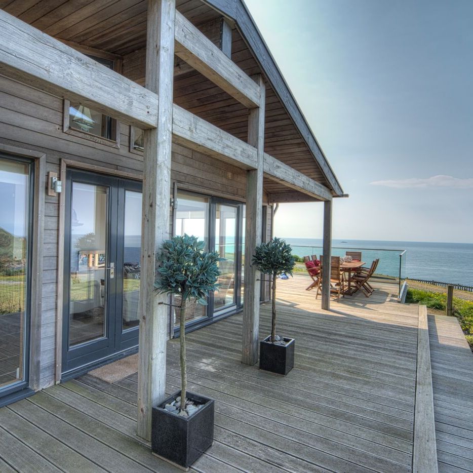 Modern wooden house with a large deck overlooking the ocean.