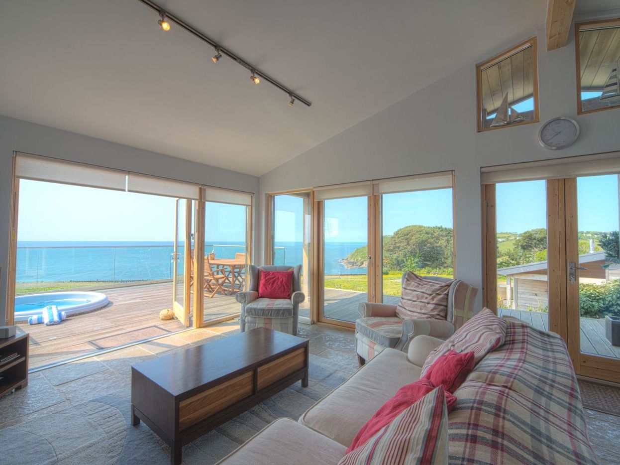 Modern living room with large windows overlooking the ocean and outdoor patio.