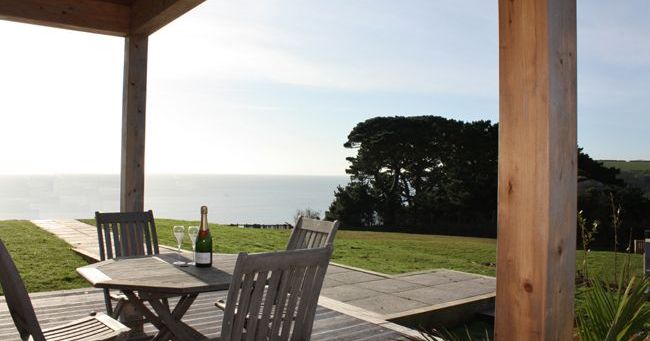 Wooden patio with table and chairs overlooking grassy lawn and ocean view.