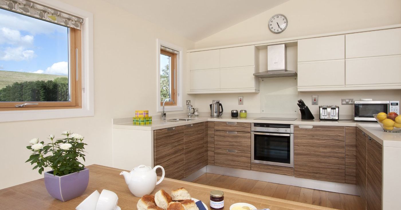 Modern kitchen with breakfast setup, featuring scones, a teapot, and a bowl of butter on a wooden table.