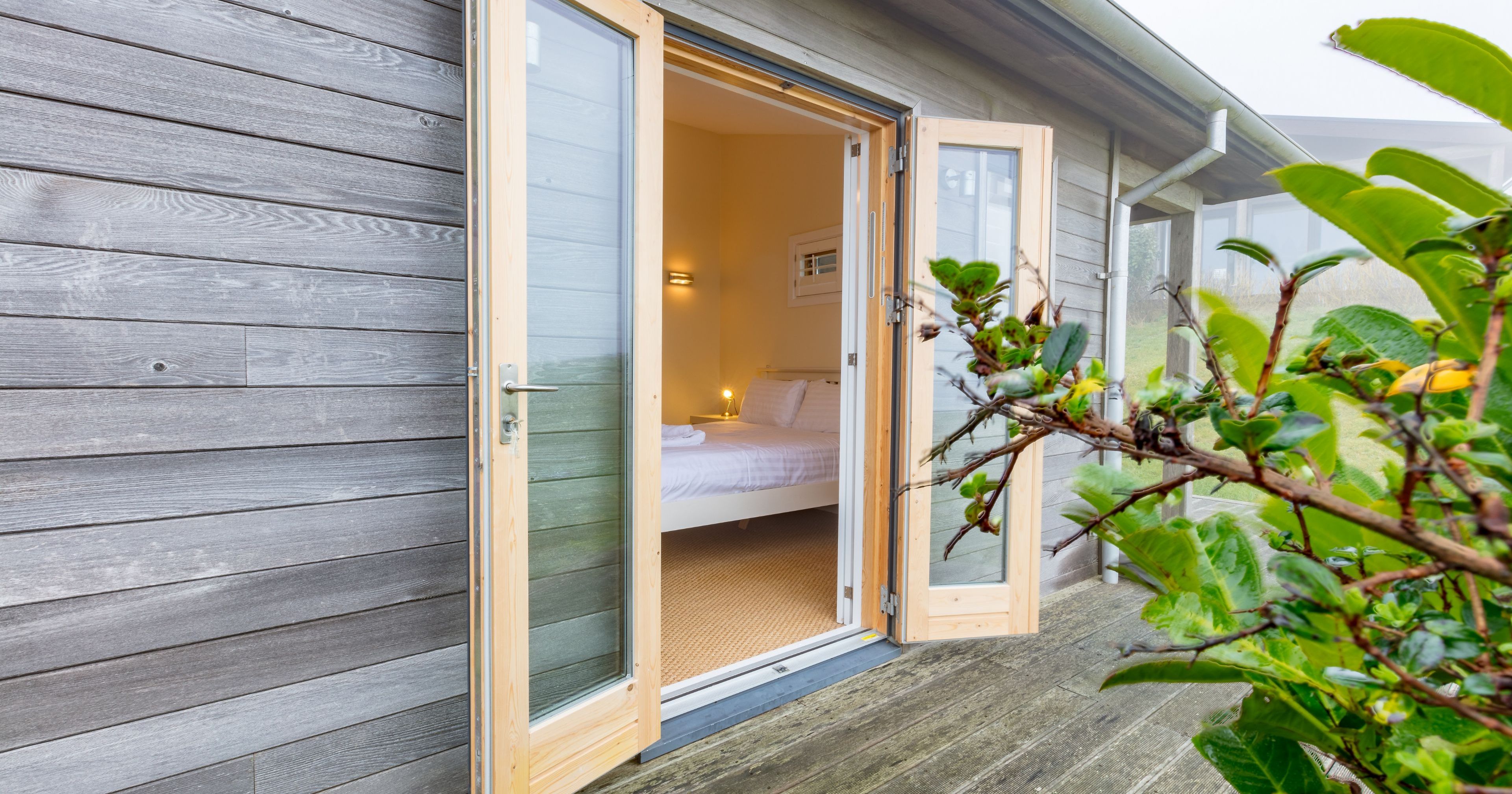 Open glass doors on a wooden cabin leading into a bedroom