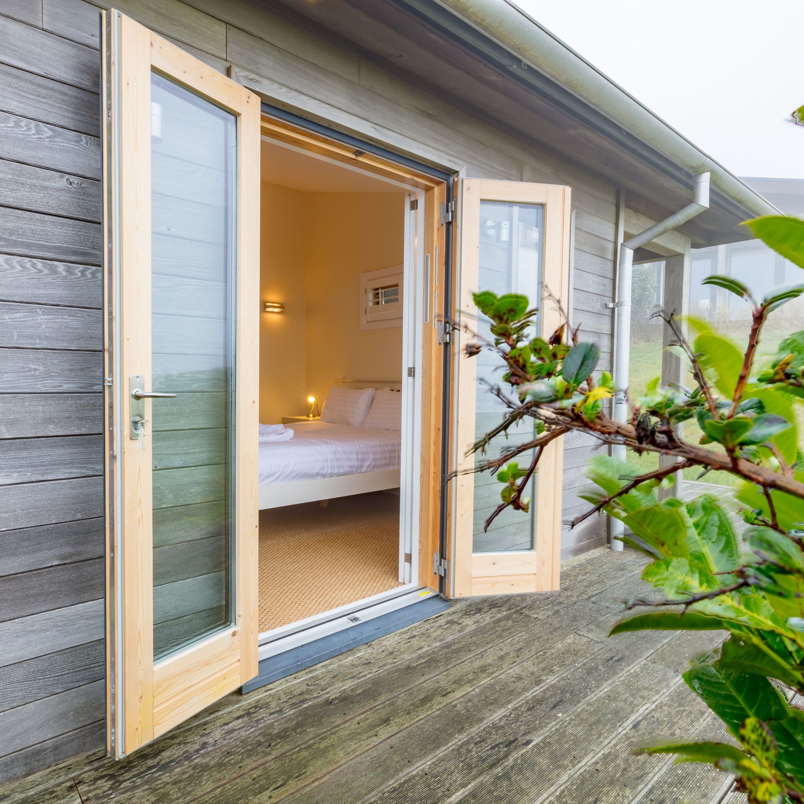 Open glass doors on a wooden cabin leading into a bedroom