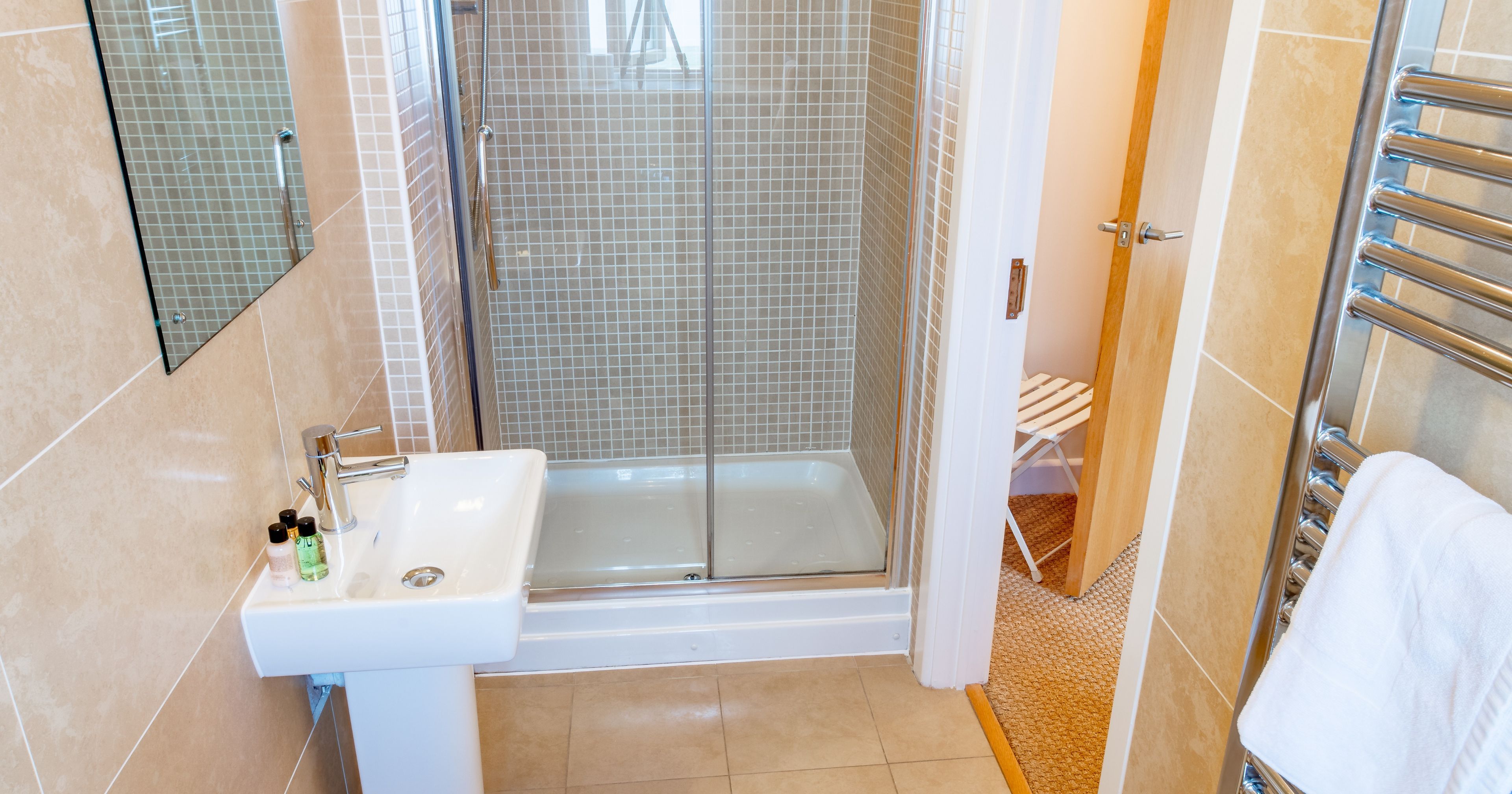 Modern bathroom with beige tiles, a glass shower, a pedestal sink, and a heated towel rack