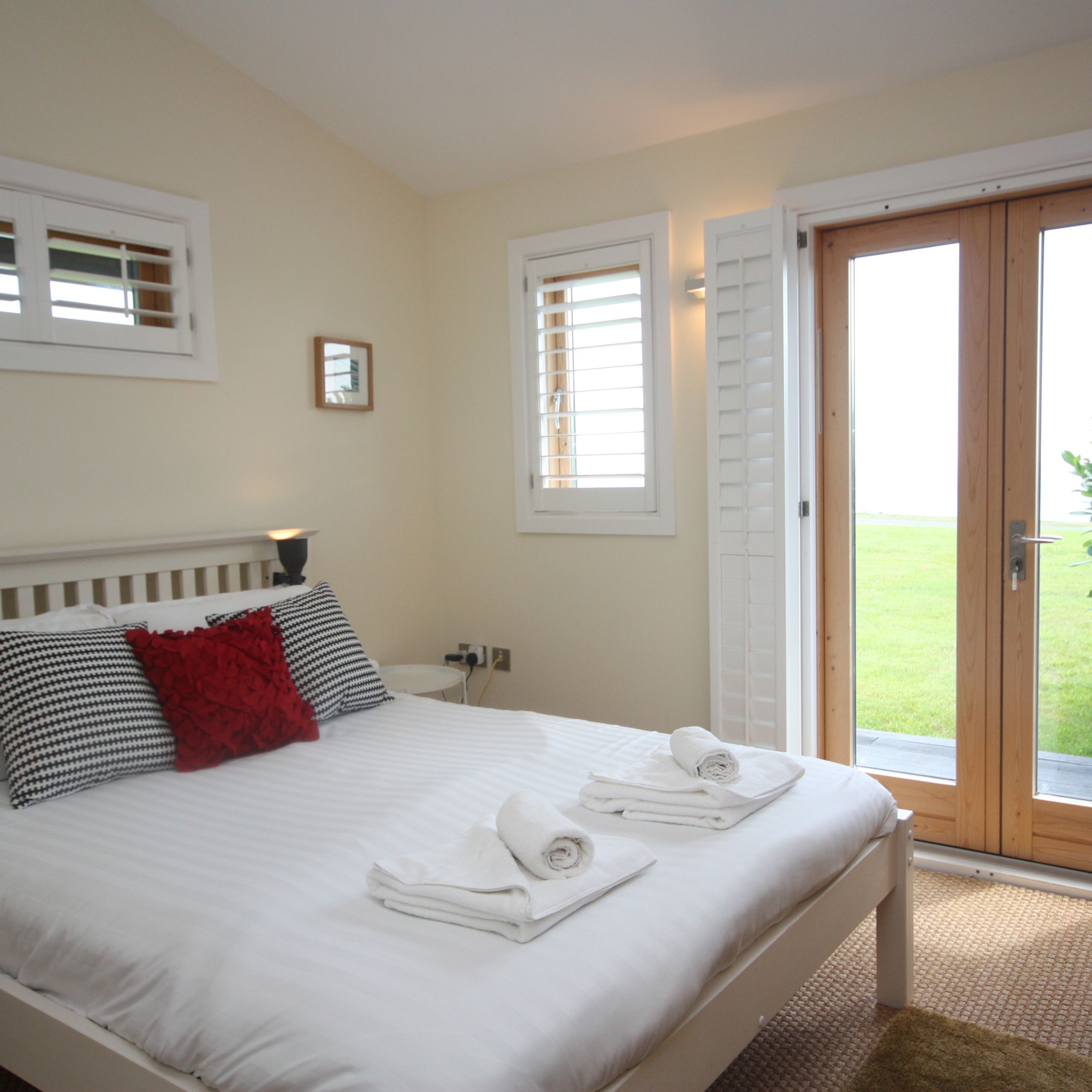 Bright bedroom with white bed linens, accent pillows, and French doors opening to a green lawn