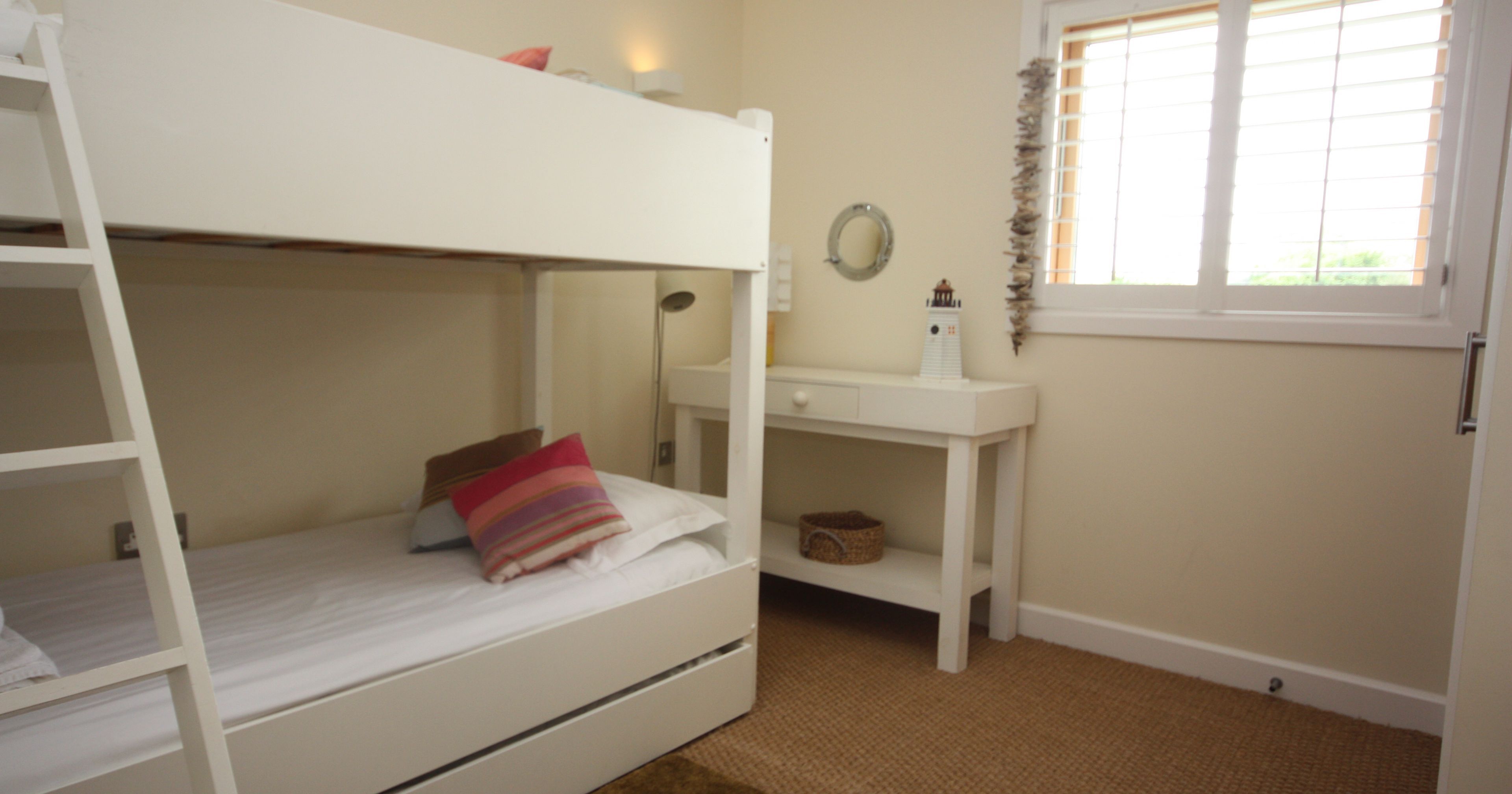 Small bedroom with white bunk bed and desk under a window.