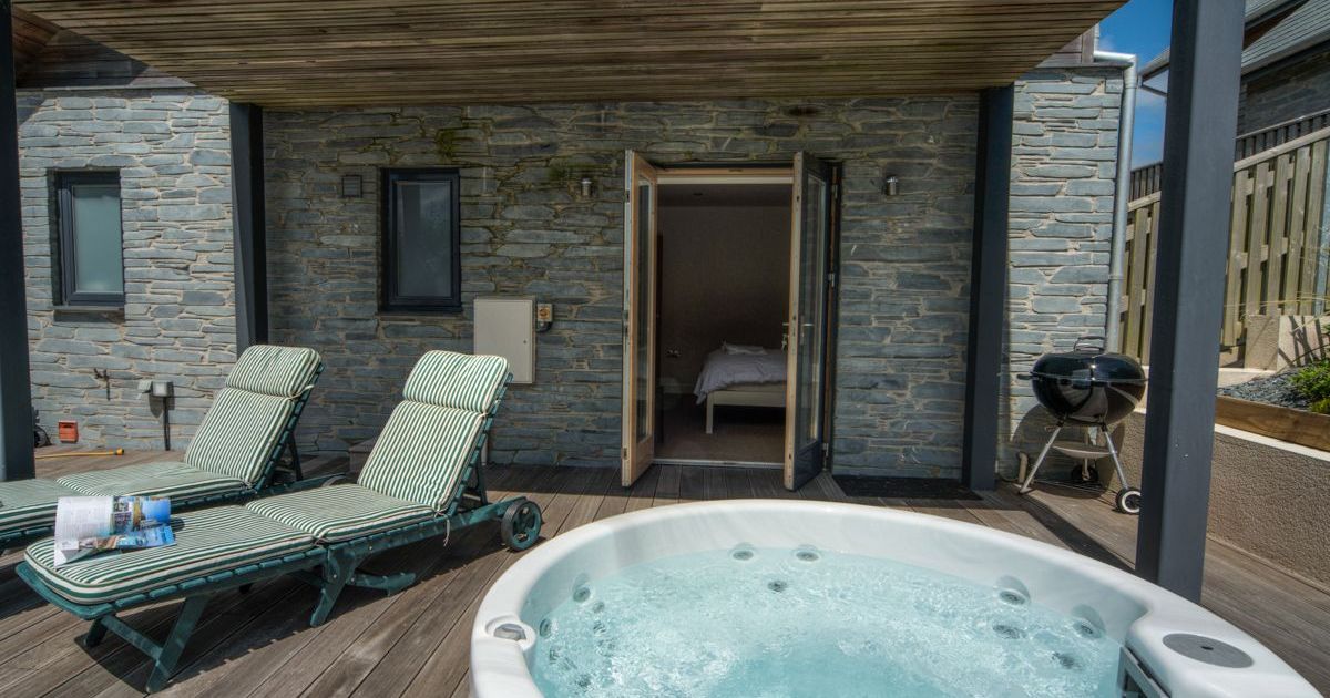 Outdoor patio with jacuzzi, lounge chairs, and a barbecue grill outside a stone building