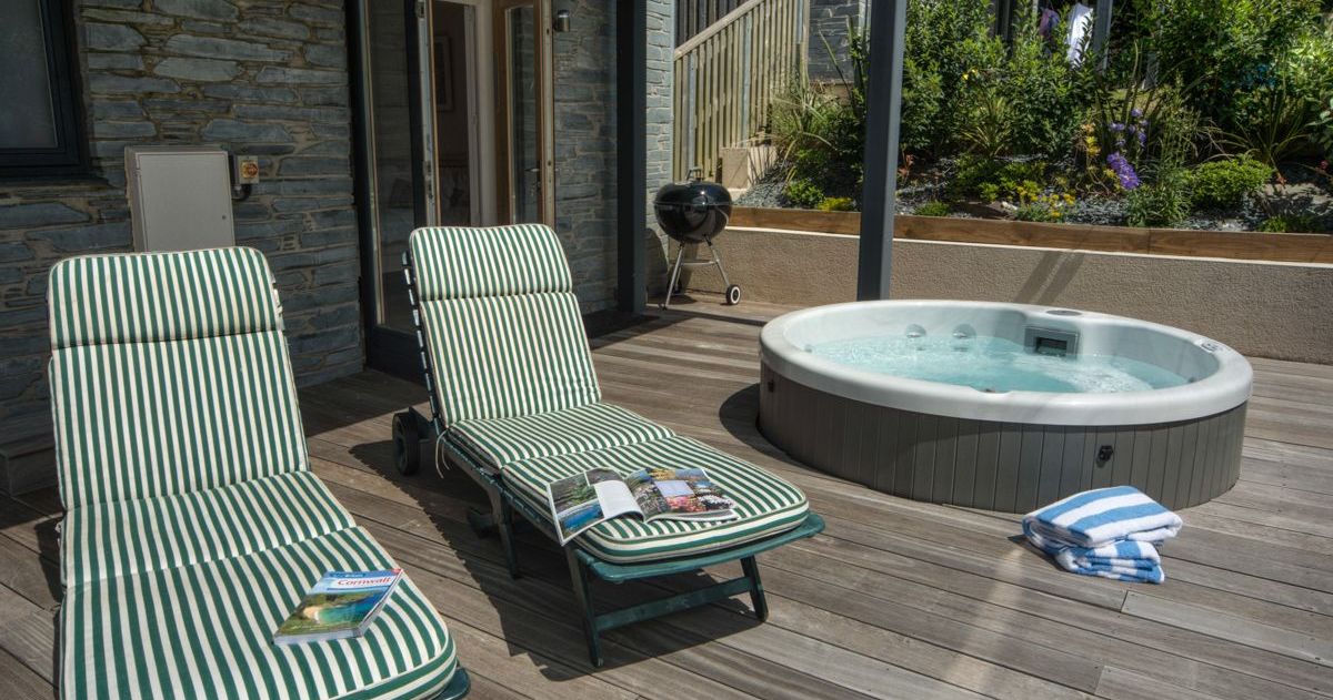 Outdoor patio with two striped lounge chairs, a hot tub, and a towel on a wooden deck