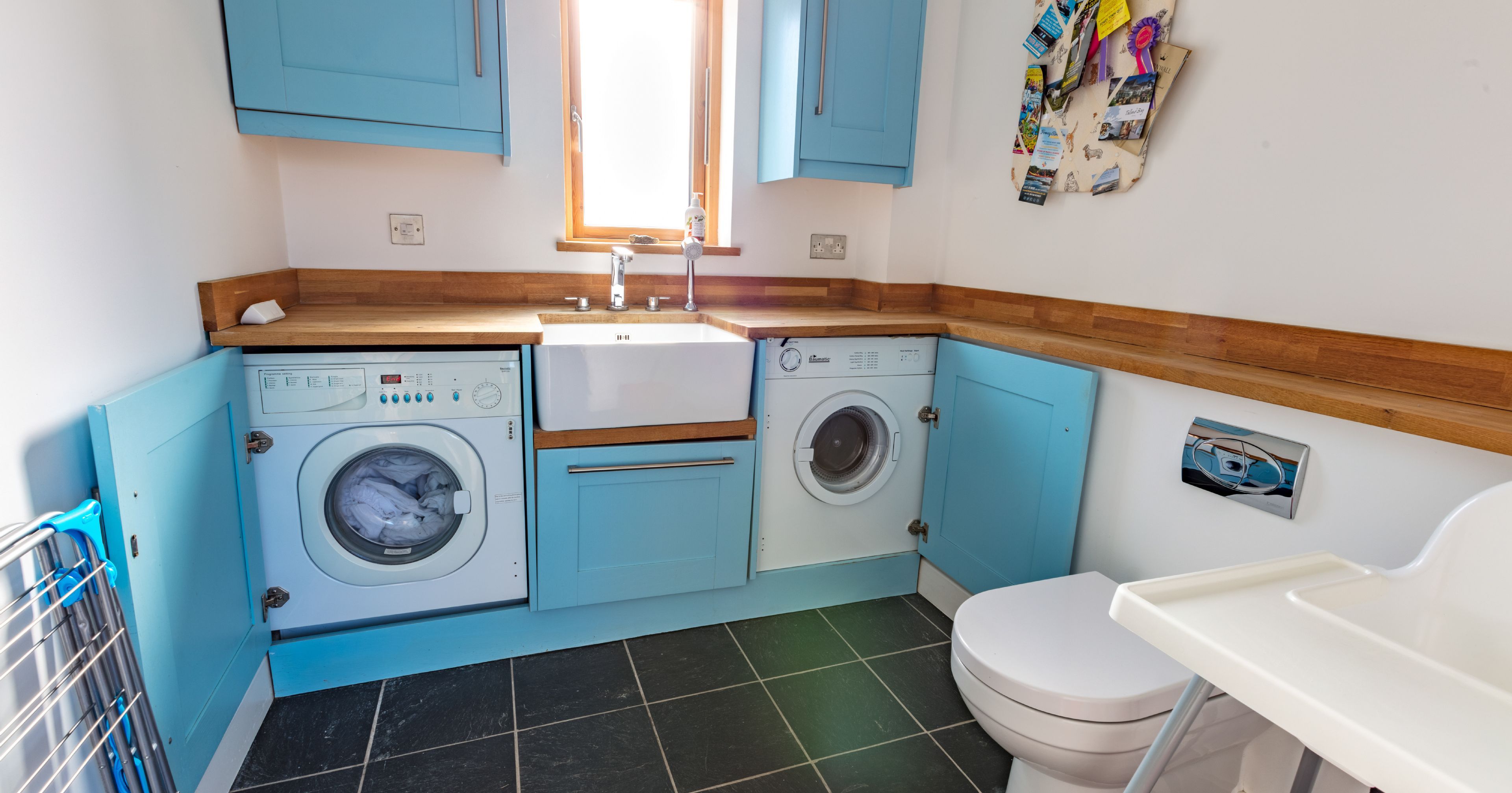 Modern laundry room with blue cabinets, washer and dryer, sink, toilet and high chair