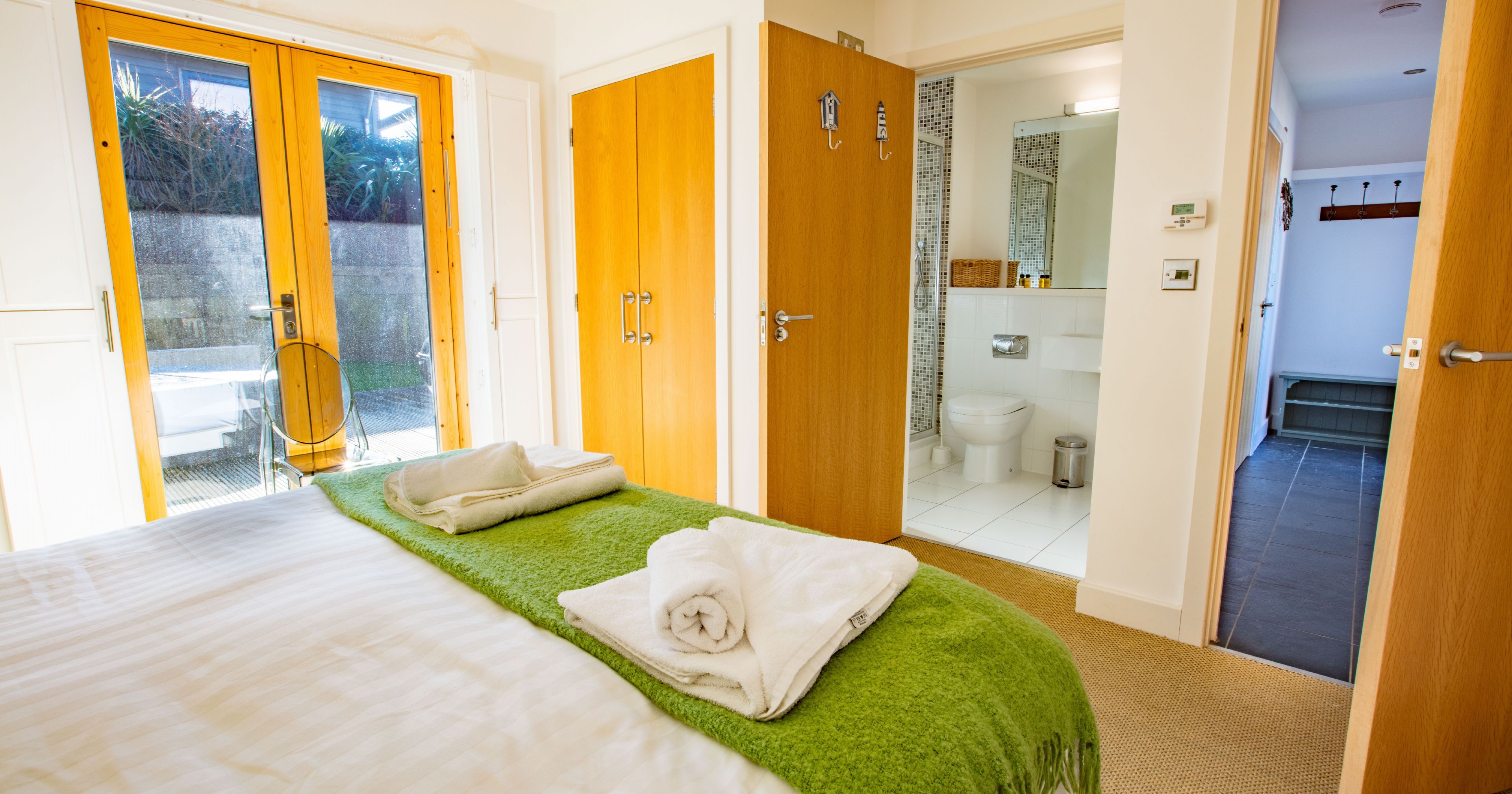 Bright modern bedroom with ensuite bathroom, patio doors, and folded towels on bed