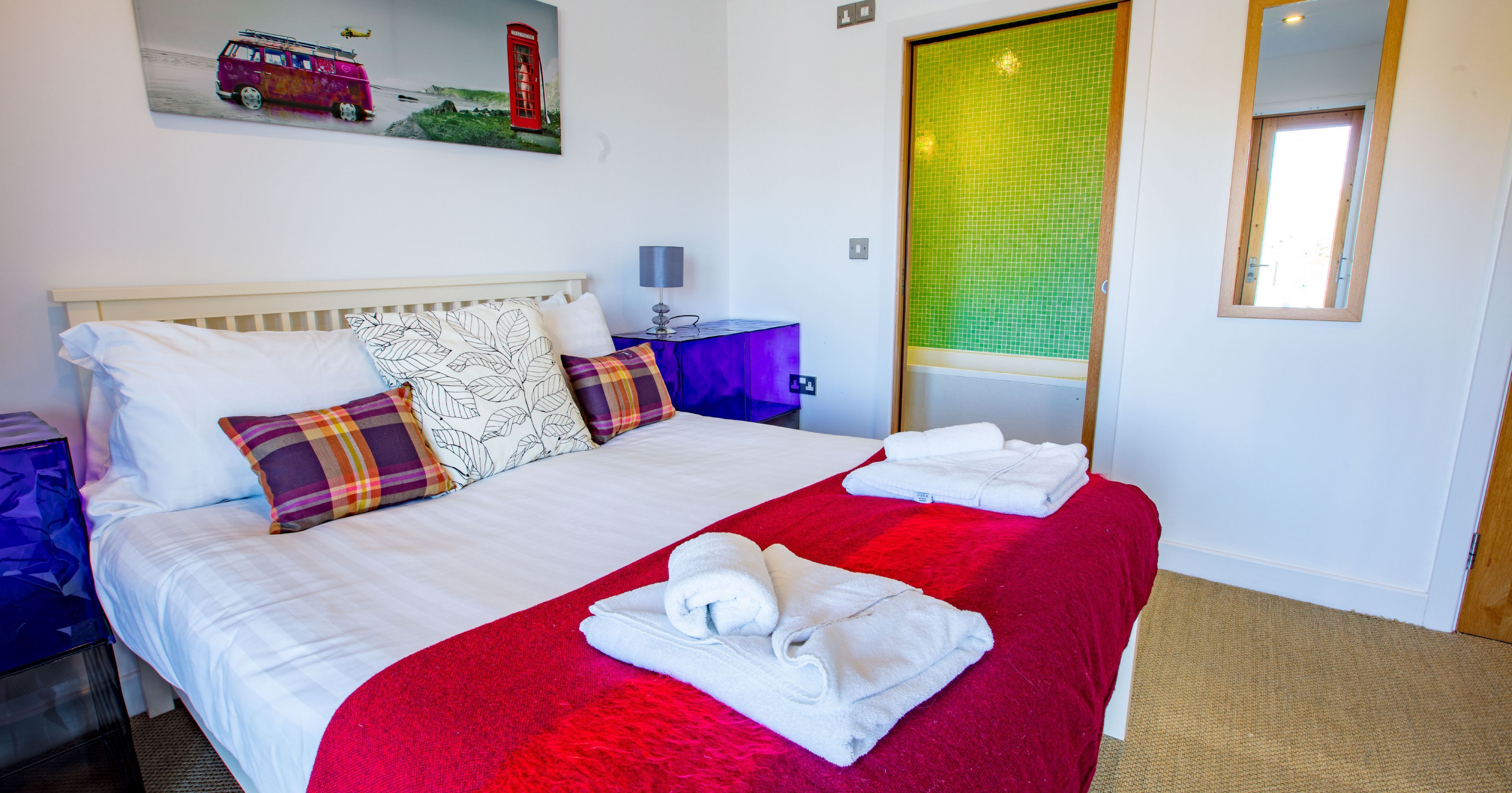 Bright modern bedroom with double bed, colorful decor, and folded towels.