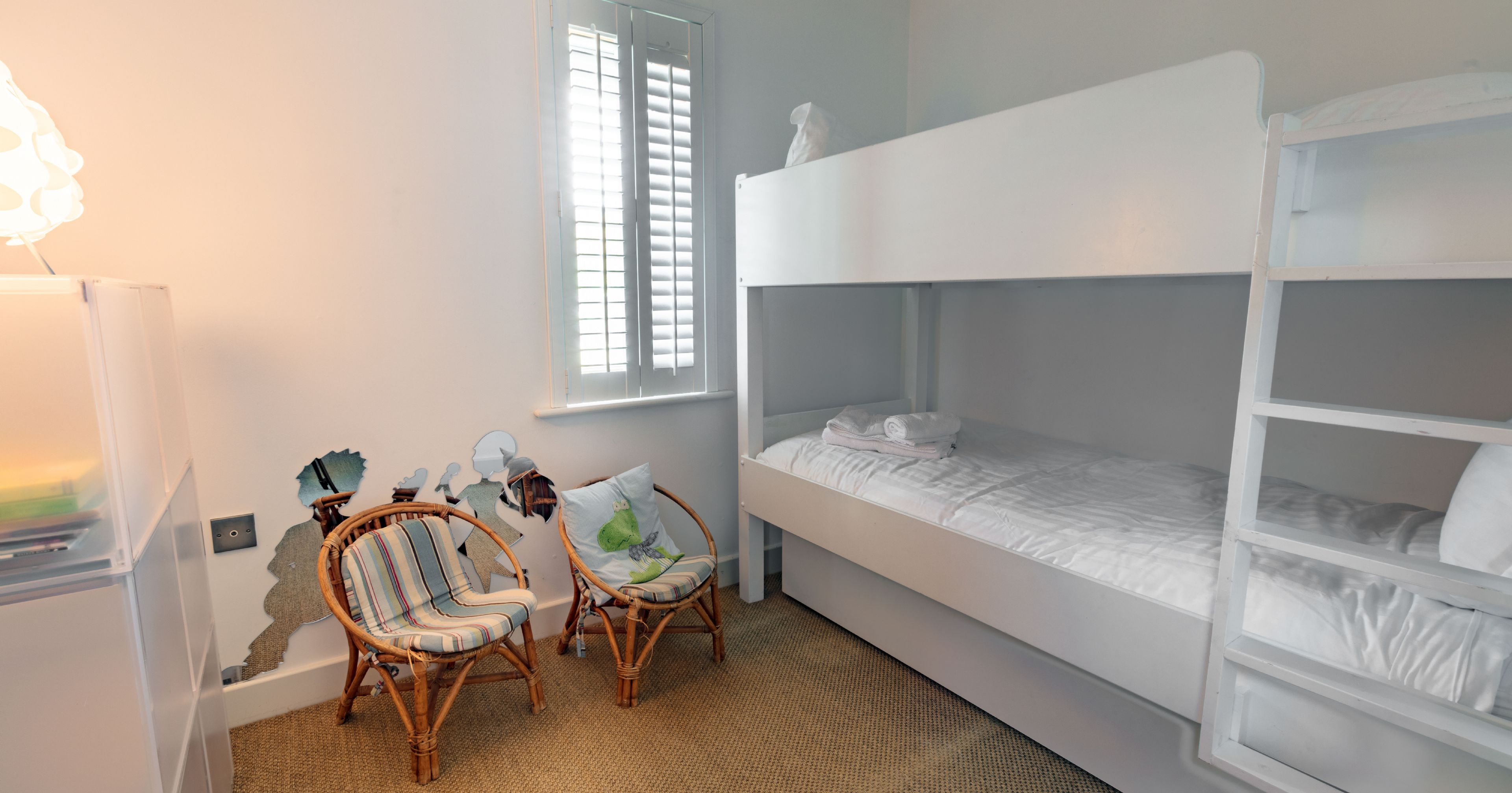 Modern children's bedroom with white bunk beds, wicker chairs, and wall art