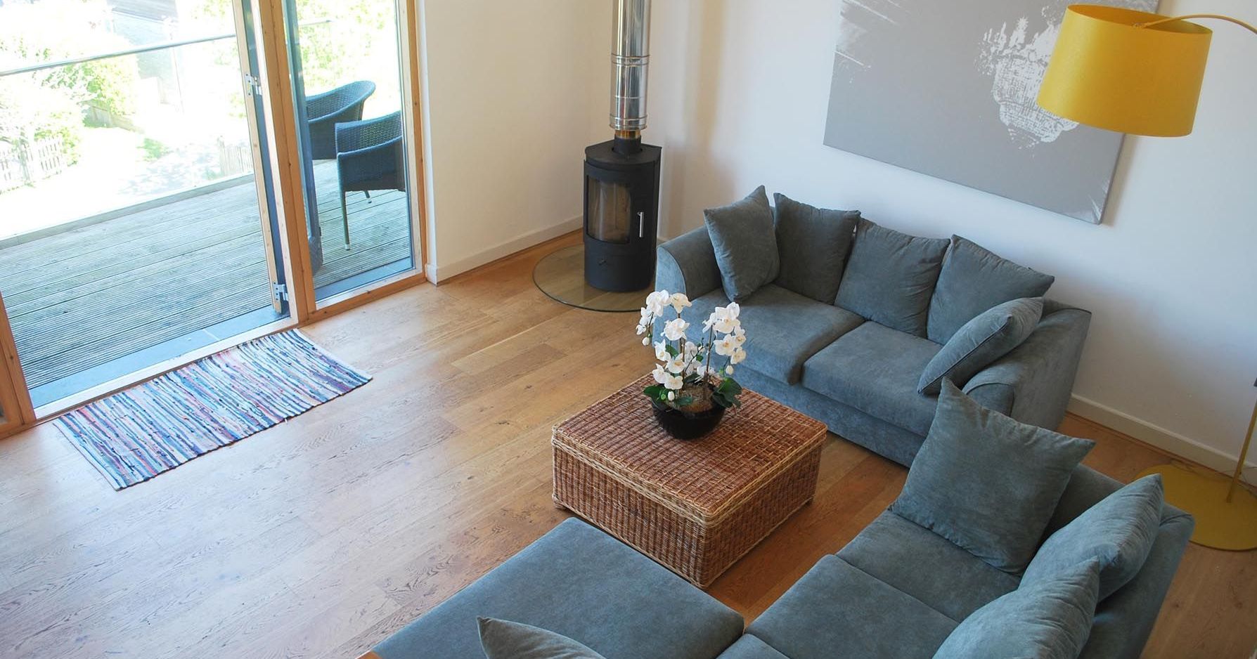 Modern living room with blue sectional sofa, rattan coffee table, and wood-burning stove