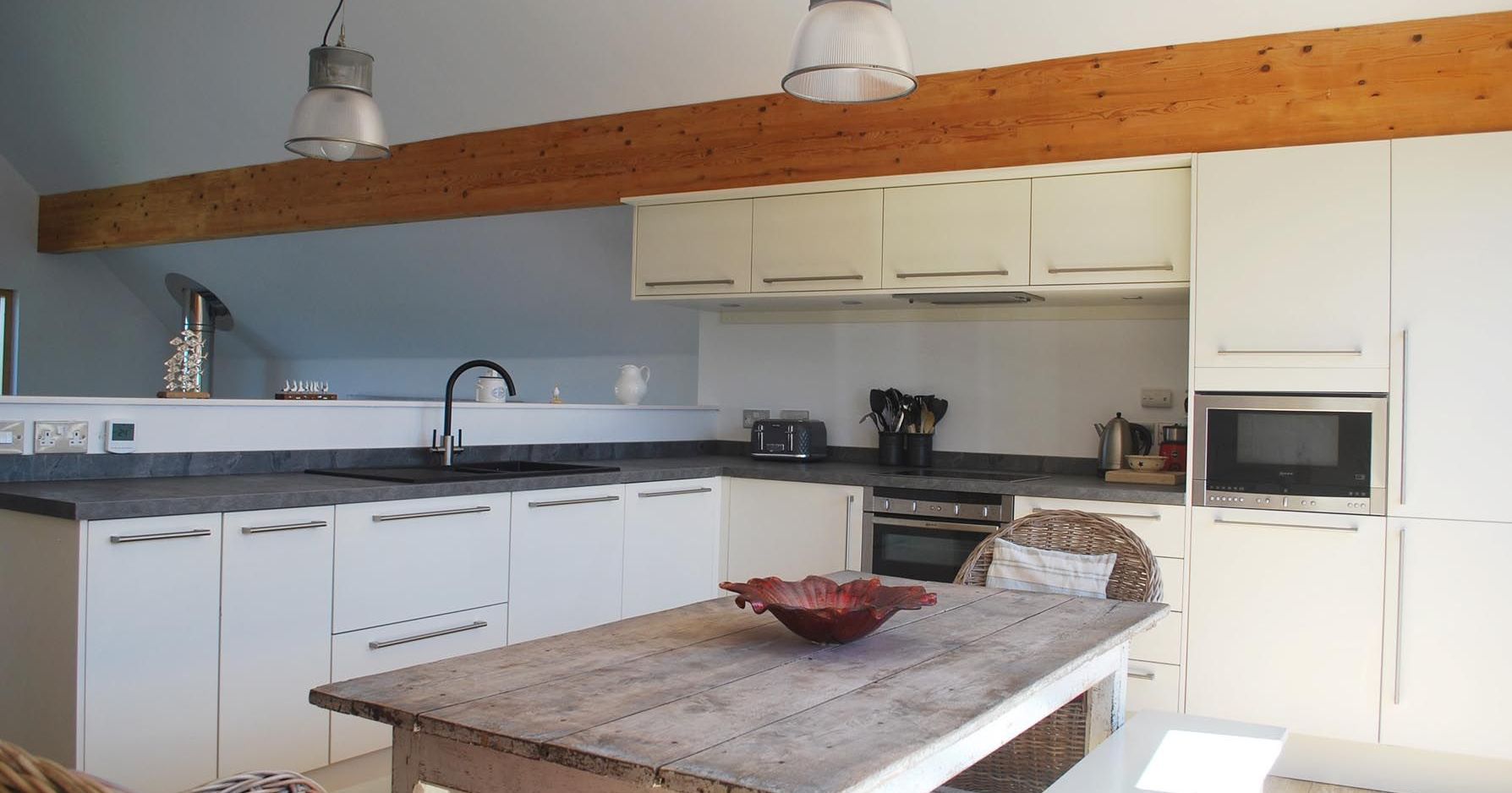 Modern kitchen with white cabinets, wooden dining table, hanging lights, and exposed wooden beam