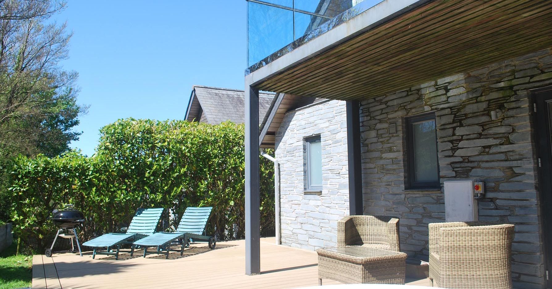 Outdoor patio area with lounge chairs, wicker seating, jacuzzi, barbecue, and stone wall house
