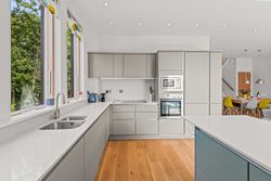 Modern kitchen with light grey cabinets, wood flooring, and large windows.