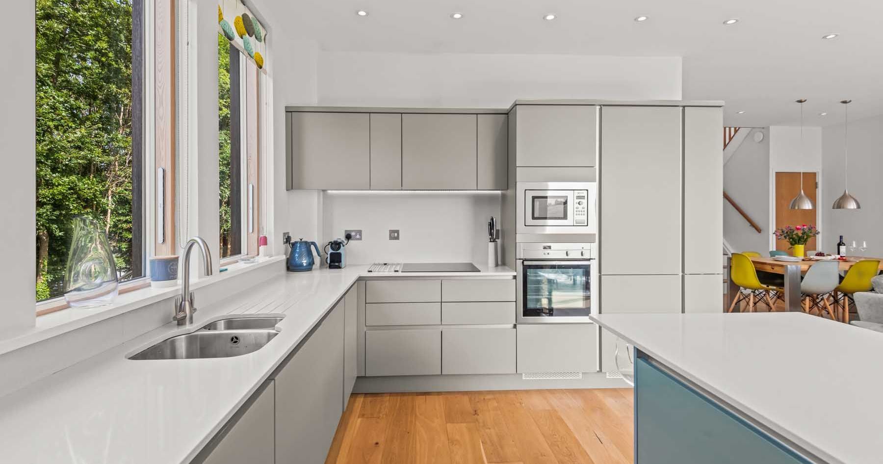 Modern kitchen with light grey cabinets, wood flooring, and large windows.
