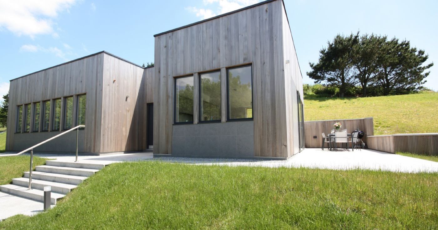 Modern house with wooden exterior and large windows surrounded by green grass