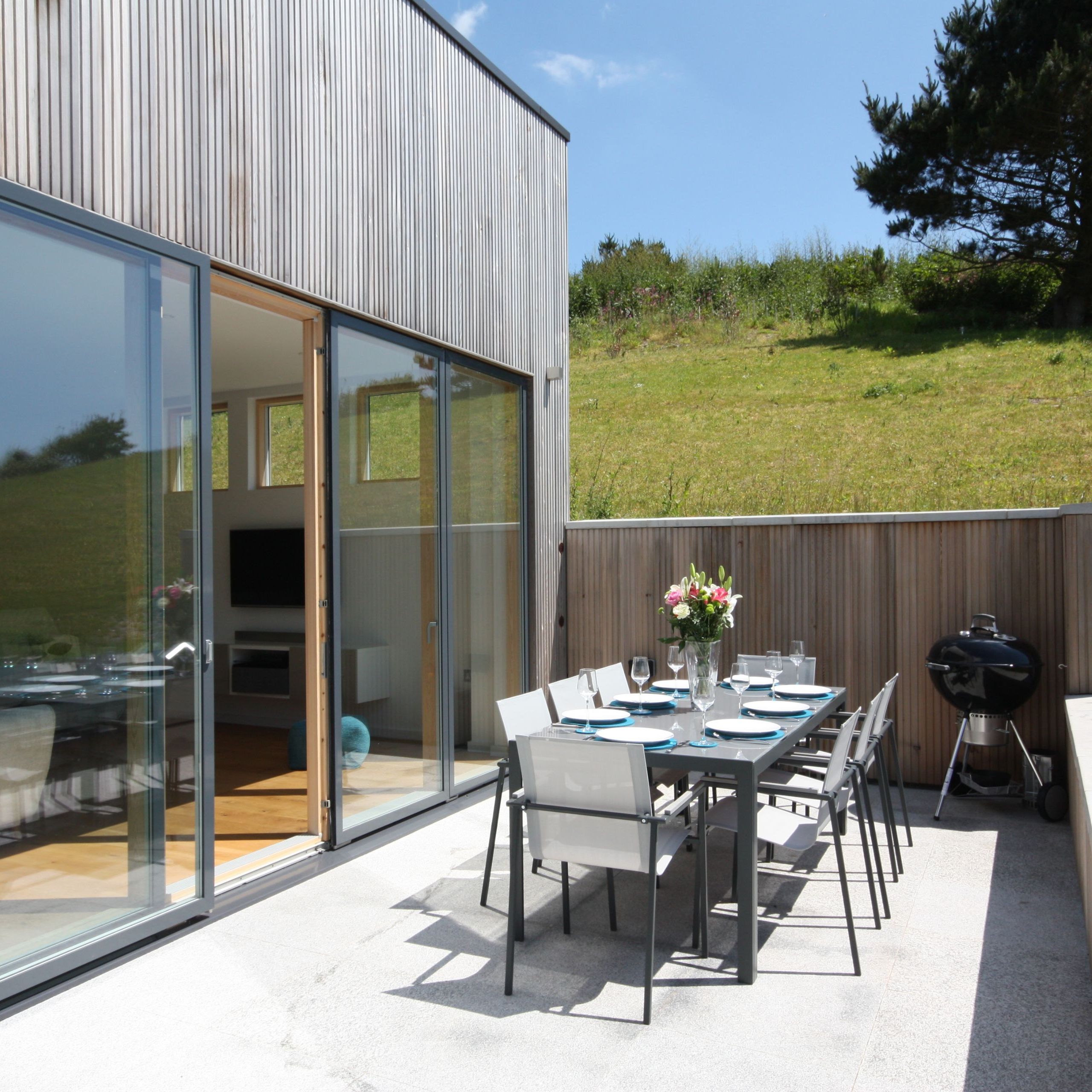 Modern outdoor patio with dining table set, barbecue, and sliding glass doors