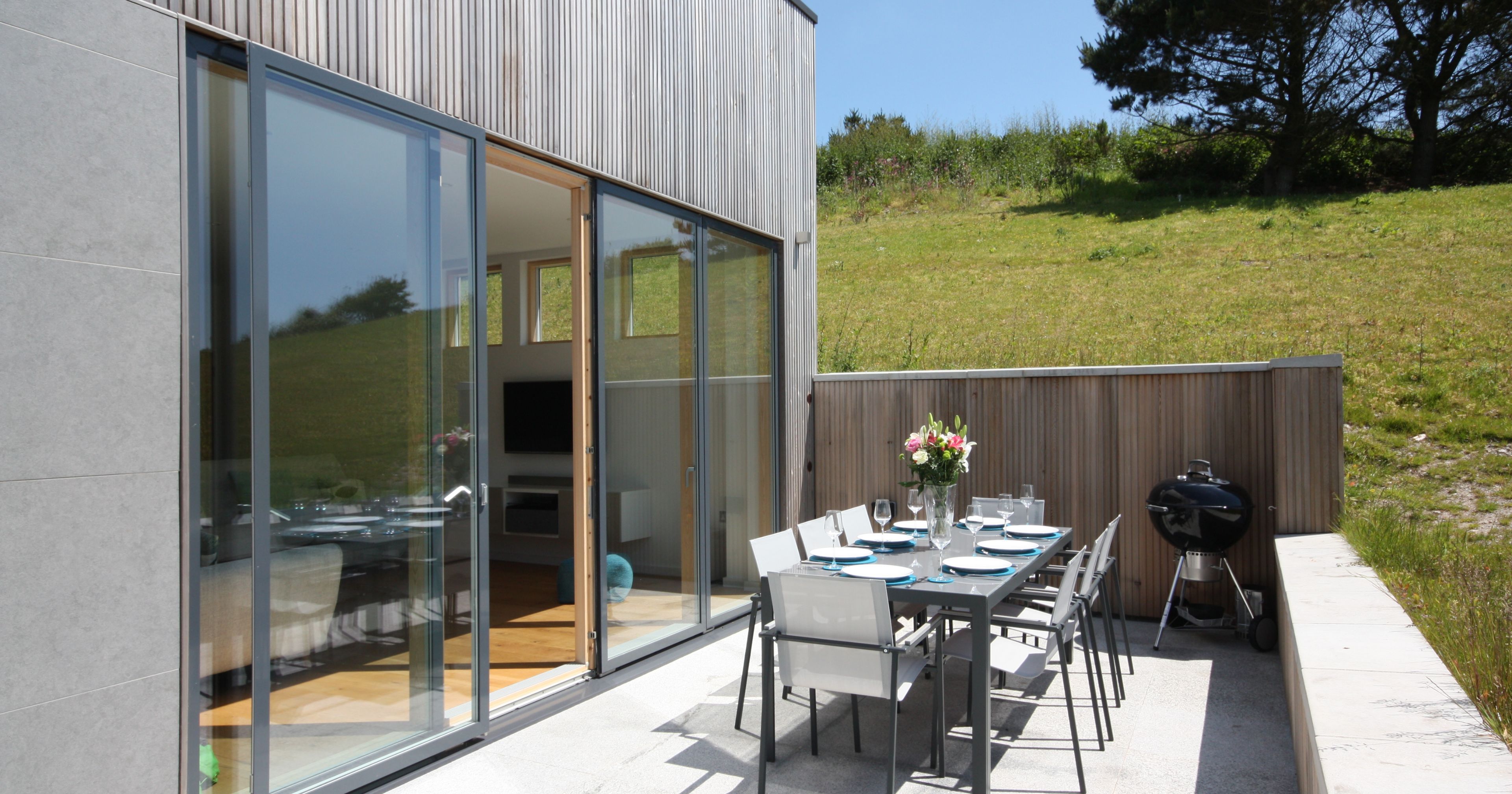 Modern outdoor patio with dining table set, barbecue, and sliding glass doors