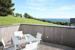 Outdoor patio table with tea set and muffins overlooking grassy hill and ocean