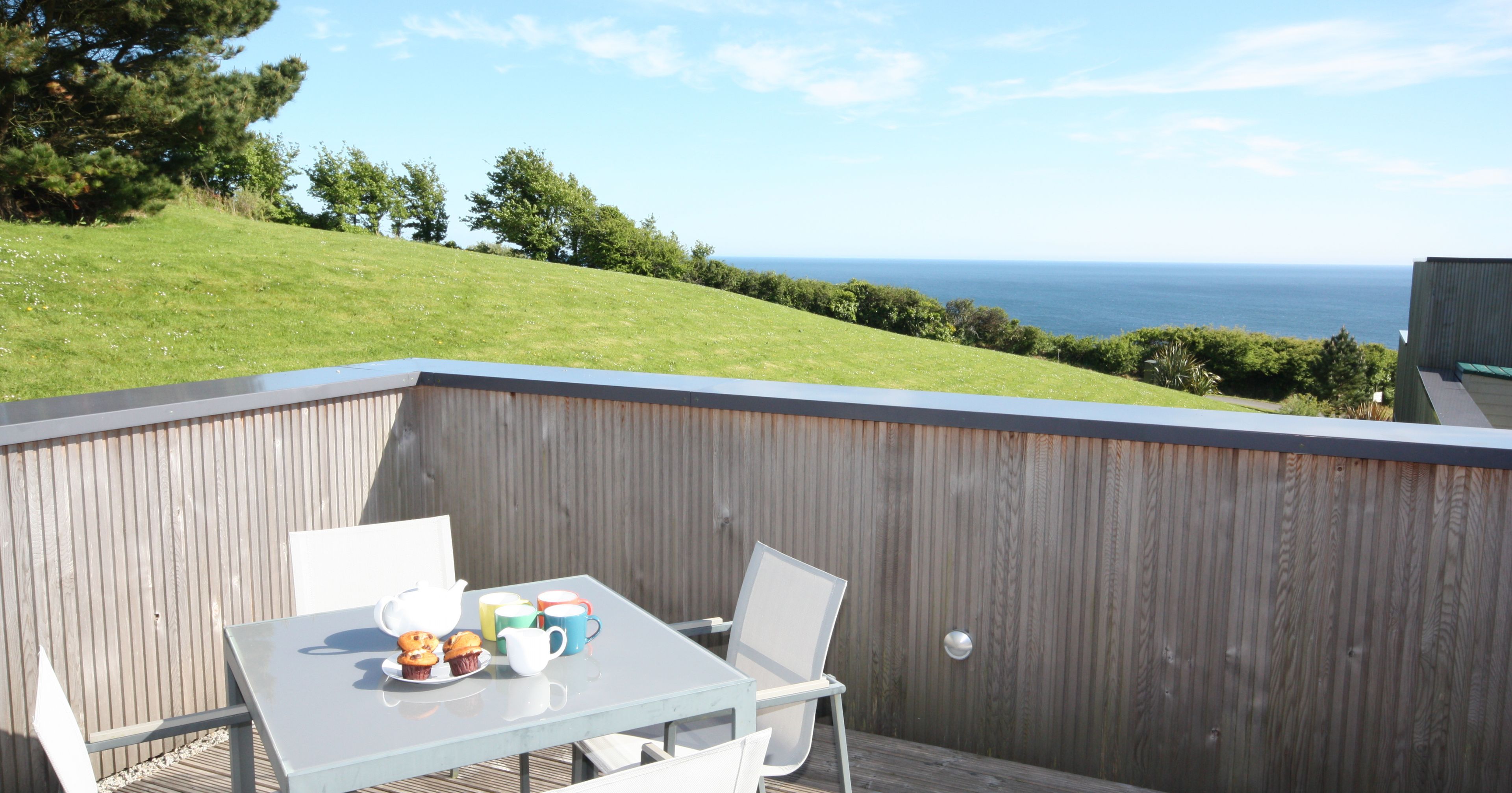 Outdoor patio table with tea set and muffins overlooking grassy hill and ocean