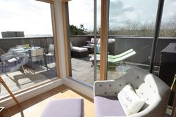 View through large windows of a sunny patio with outdoor furniture including chairs, a table, and loungers.
