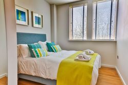 Modern bedroom with teal and yellow decor and large windows with blinds