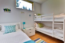 Modern children's bedroom with a single bed and a bunk bed, decorated in white with blue and green accents.