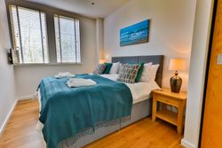 Modern bedroom with a teal blanket, large windows, and bedside lamp