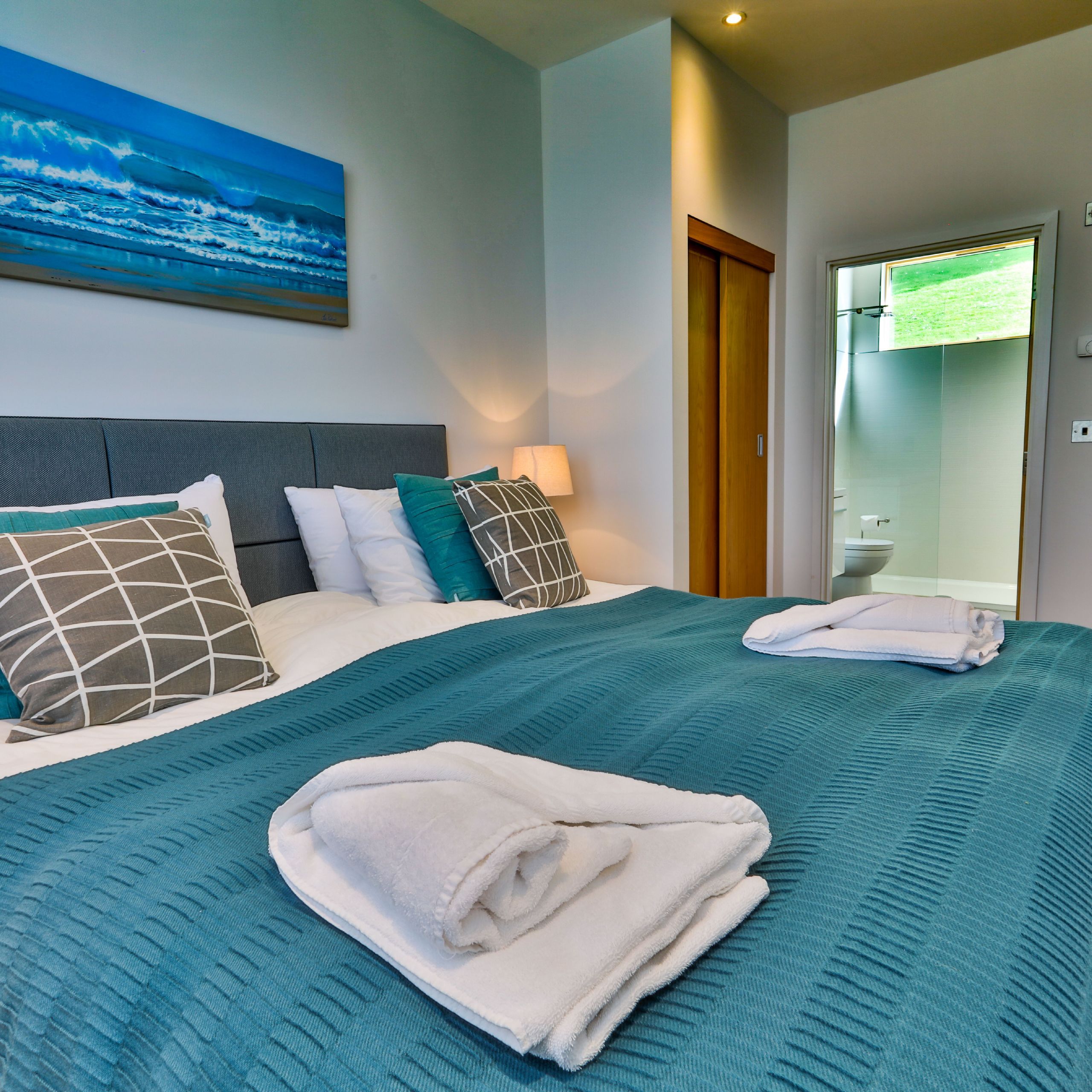 Modern bedroom with teal bedding, pillows, and towels arranged on the bed.