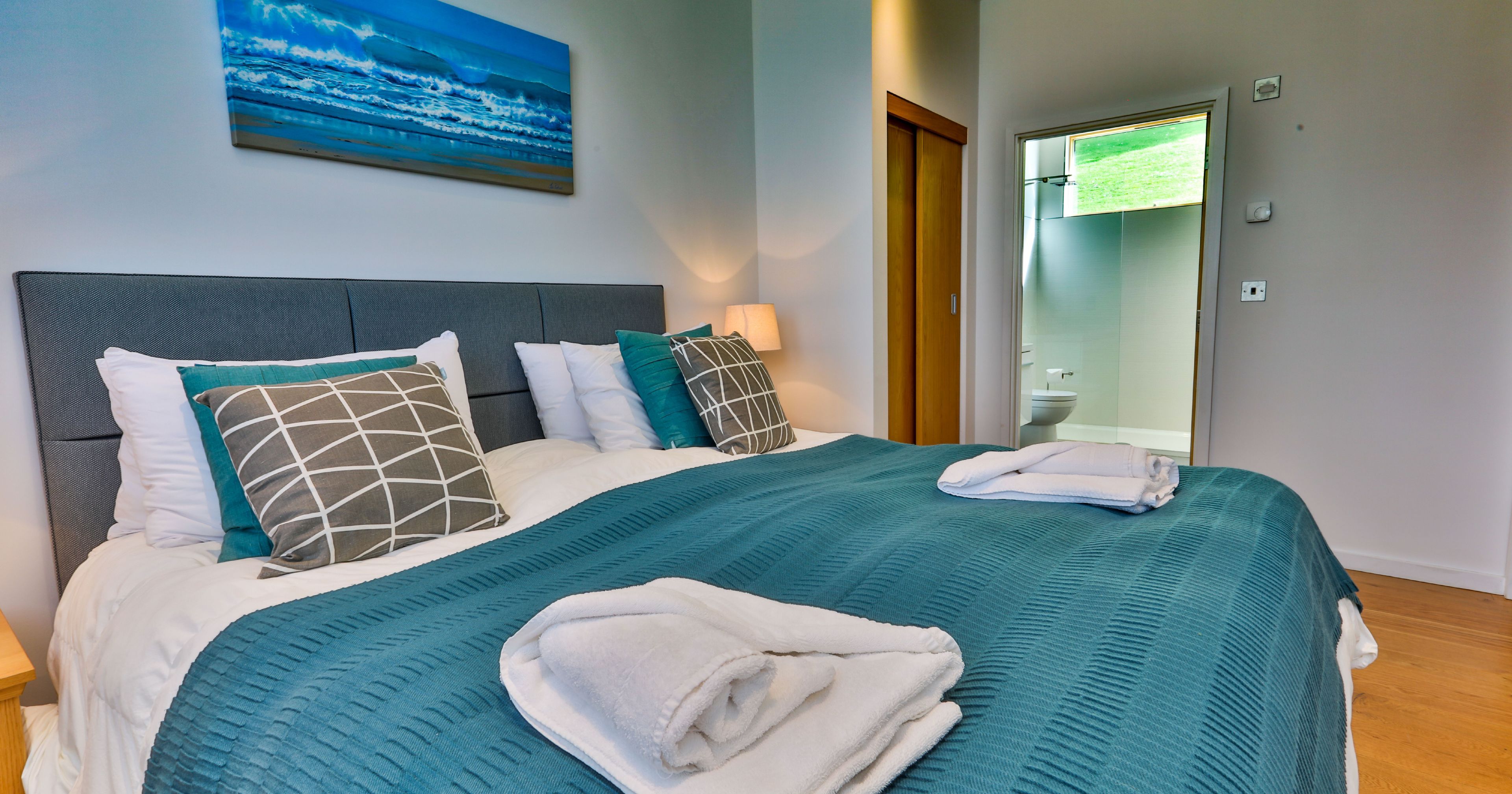 Modern bedroom with teal bedding, pillows, and towels arranged on the bed.