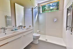 Modern bathroom with double sink, walk-in shower, toilet, and large window.