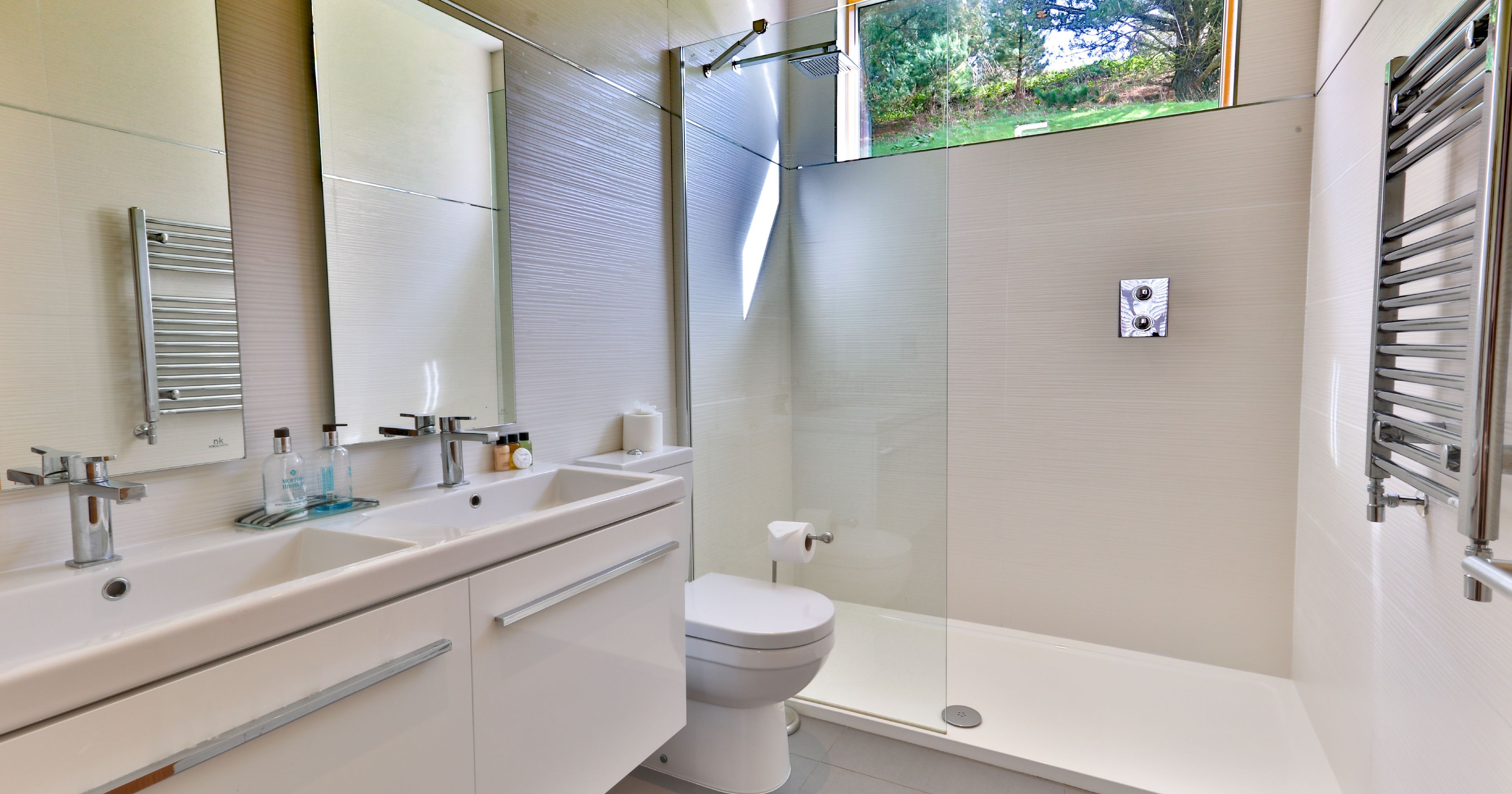 Modern bathroom with double sink, walk-in shower, toilet, and large window.