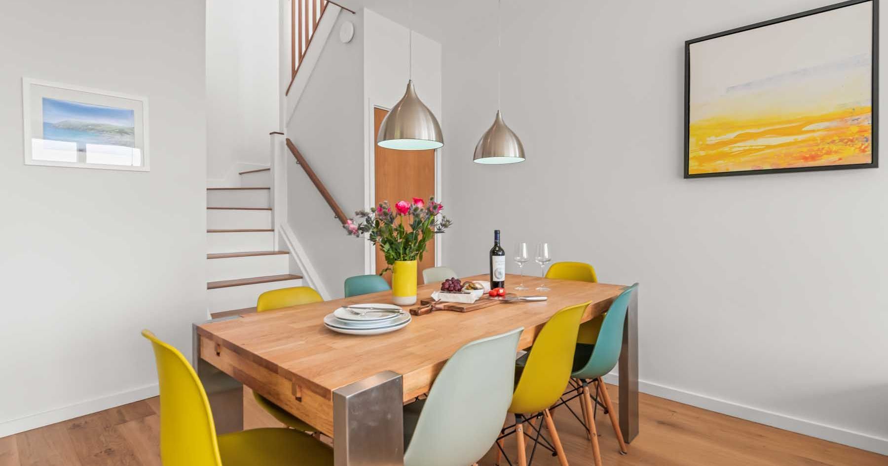 Modern dining room with wooden table, colorful chairs, and pendant lights