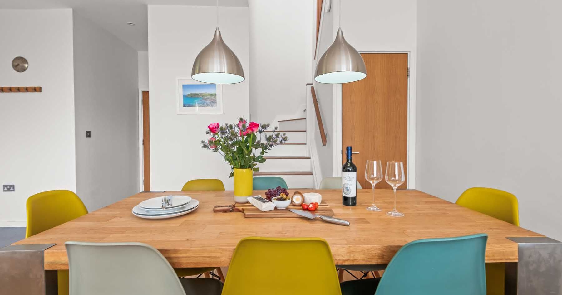 Modern dining room with wooden table, colorful chairs, and pendant lights