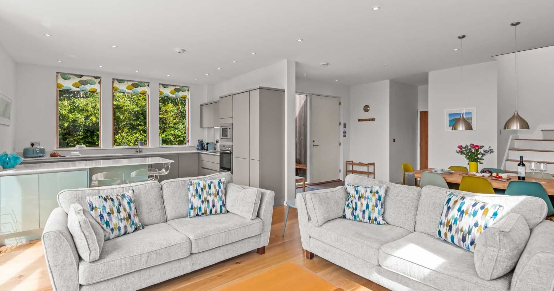 Modern open plan living room and kitchen with large windows and contemporary furniture.