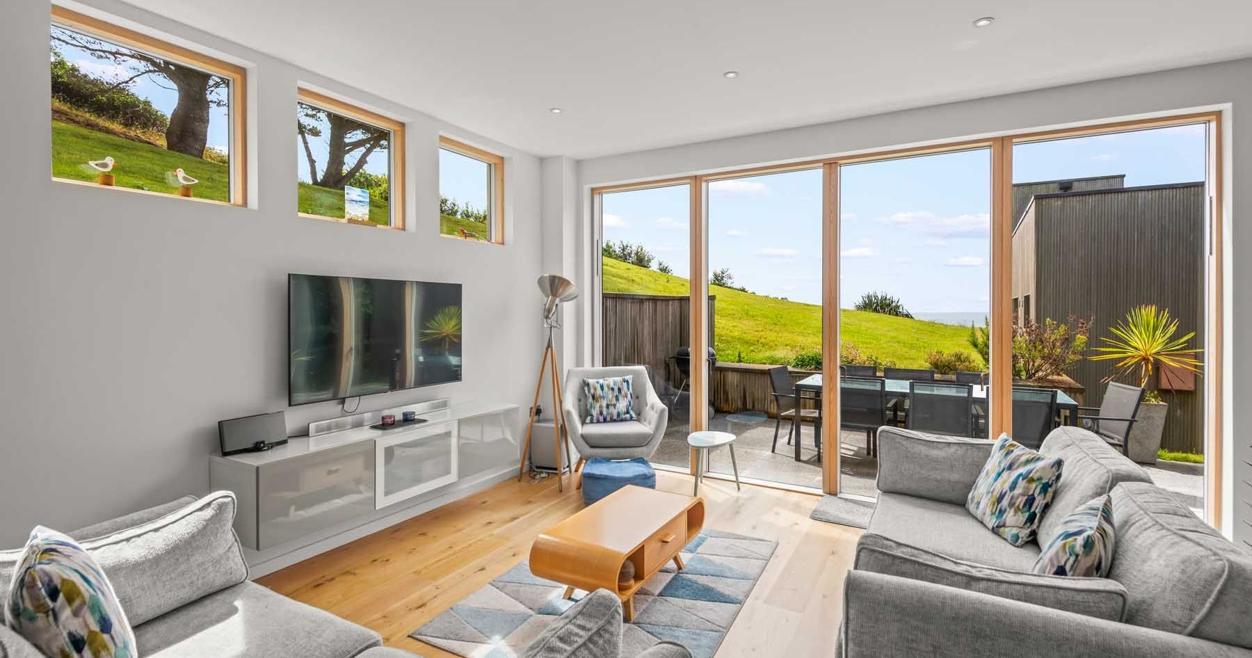 Modern living room with large windows overlooking a green garden and outdoor dining area.