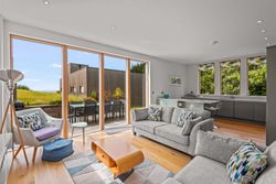 Modern open plan living room and kitchen with large windows and patio doors overlooking a green garden.