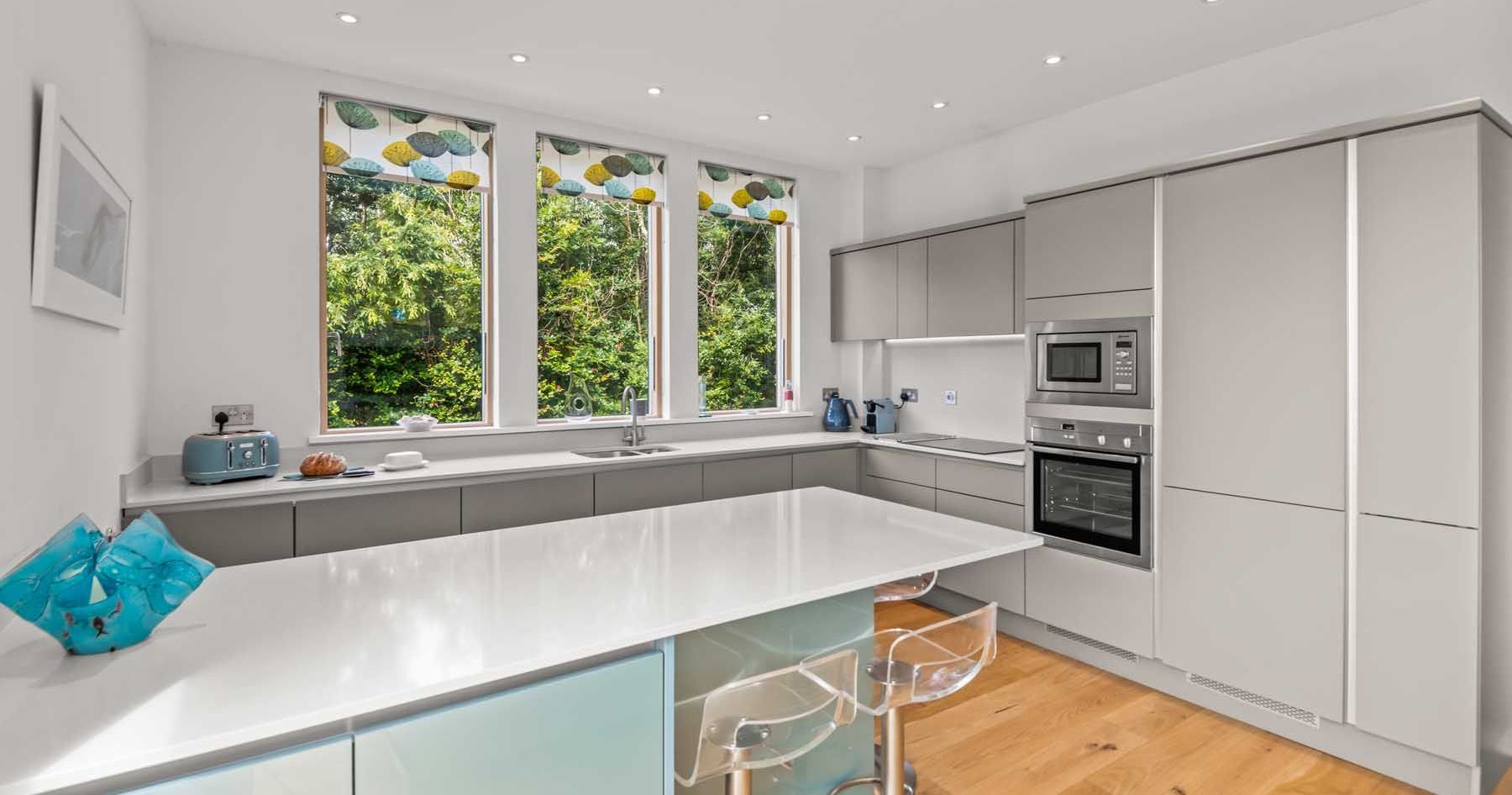 Modern kitchen with white countertops, light grey cabinets, and large windows.