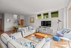 Modern living room and dining area with light grey sofas, flat screen TV, and large windows.