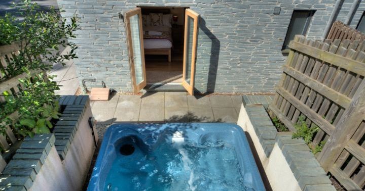 Outdoor hot tub in a private walled patio area with open doors leading to a bedroom inside a stone house.
