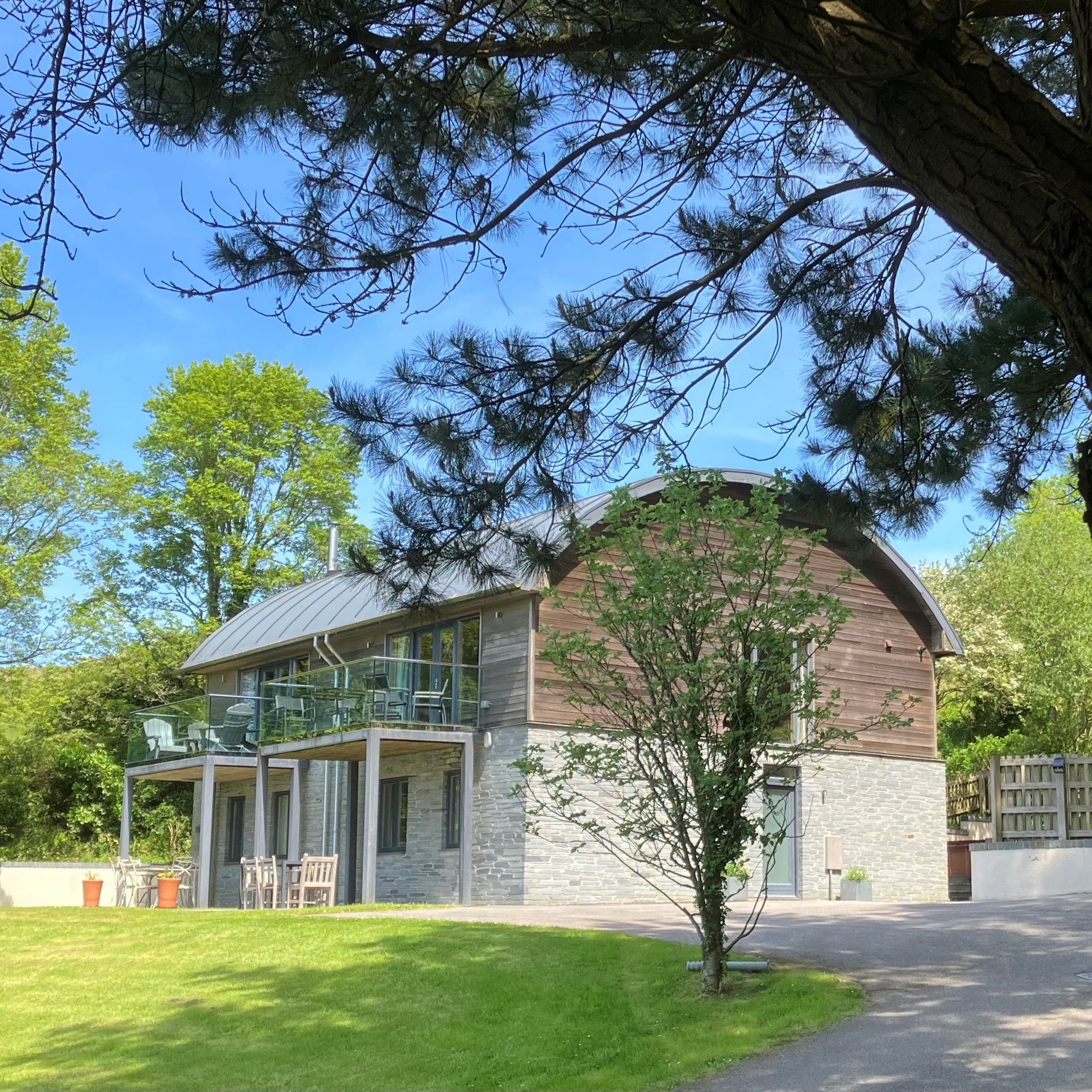 Modern two-story house with wood and stone facade, surrounded by trees and green lawn
