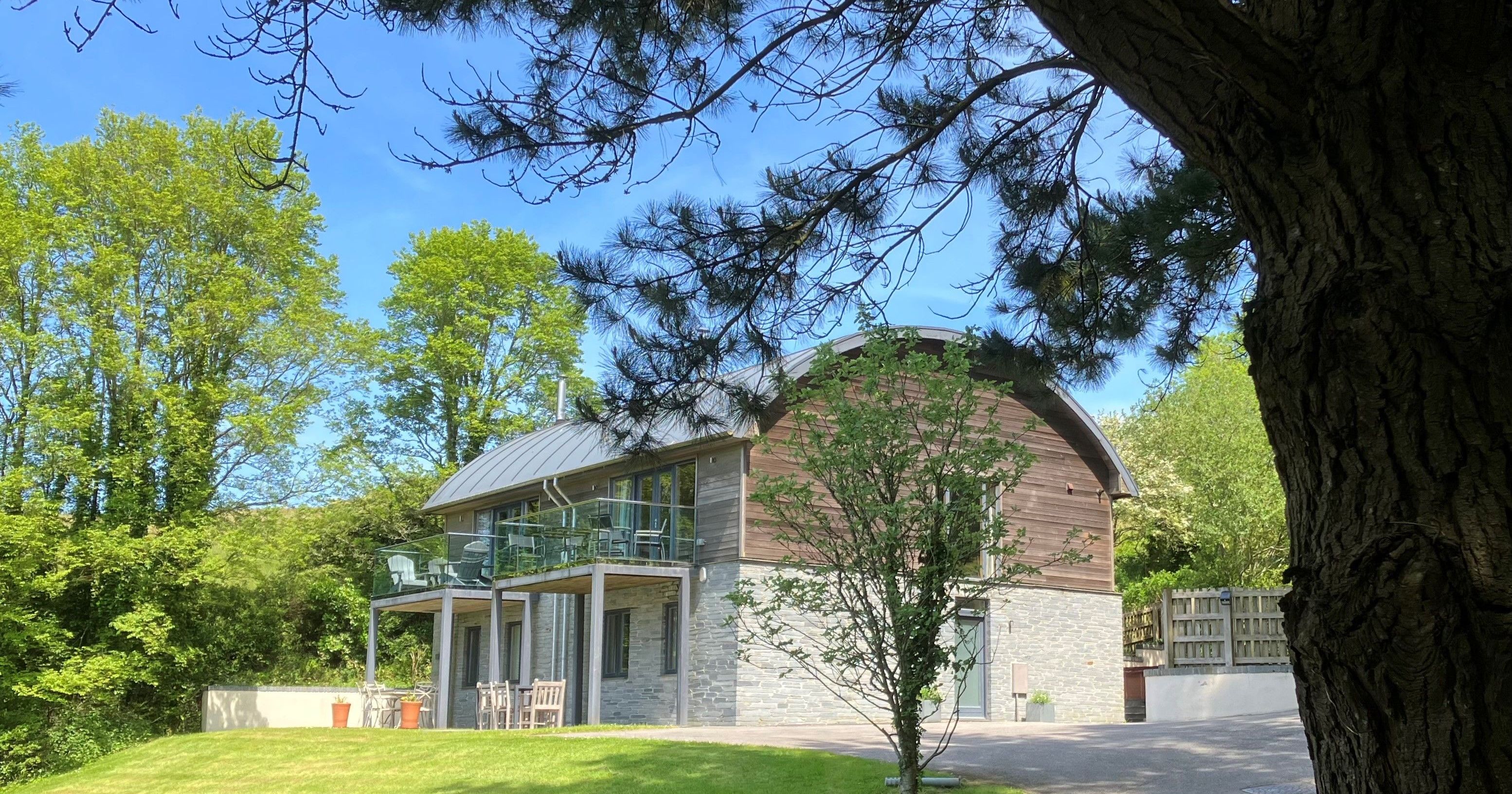 Modern two-story house with wood and stone facade, surrounded by trees and green lawn