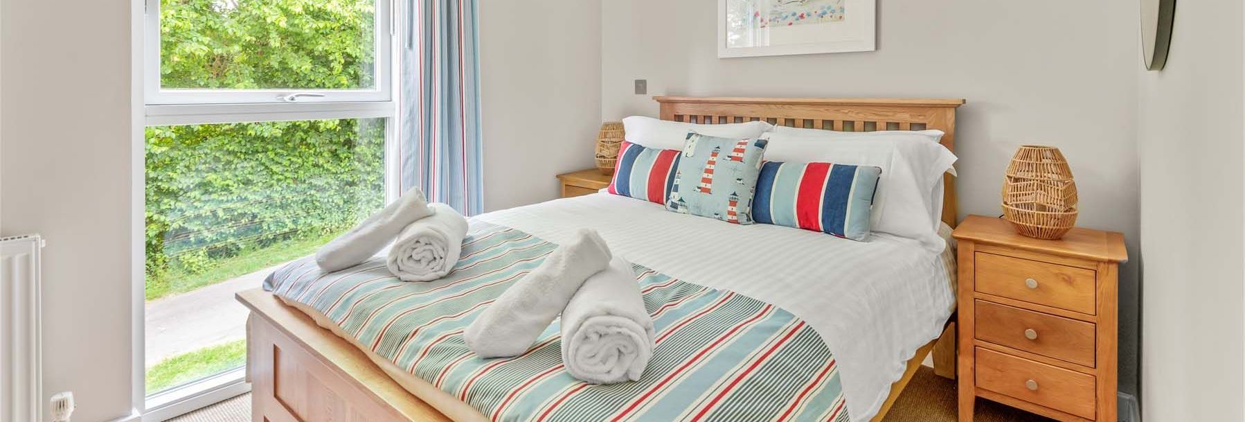 Bright and cozy bedroom with a wooden bed, striped bedding, colorful pillows, and large window with a garden view.