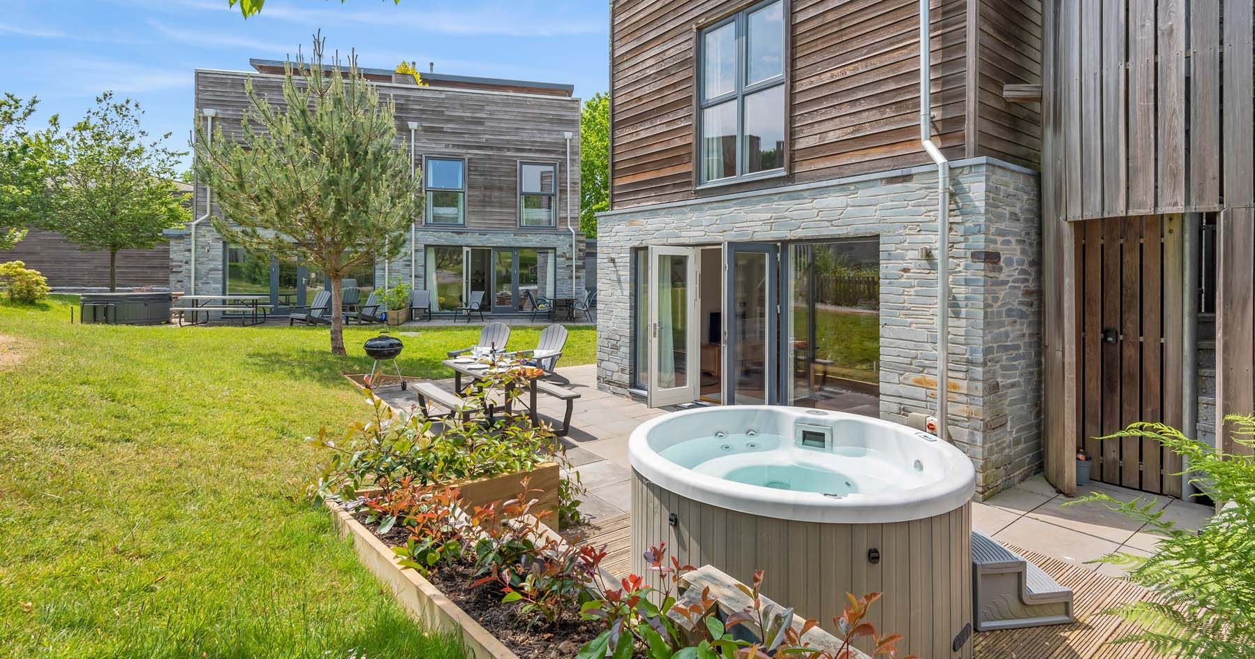 Modern house with wooden exterior, hot tub and patio seating in a sunny garden