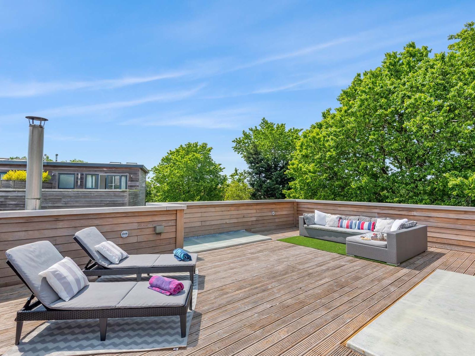 Rooftop deck with lounge chairs and a sofa, surrounded by trees and a blue sky