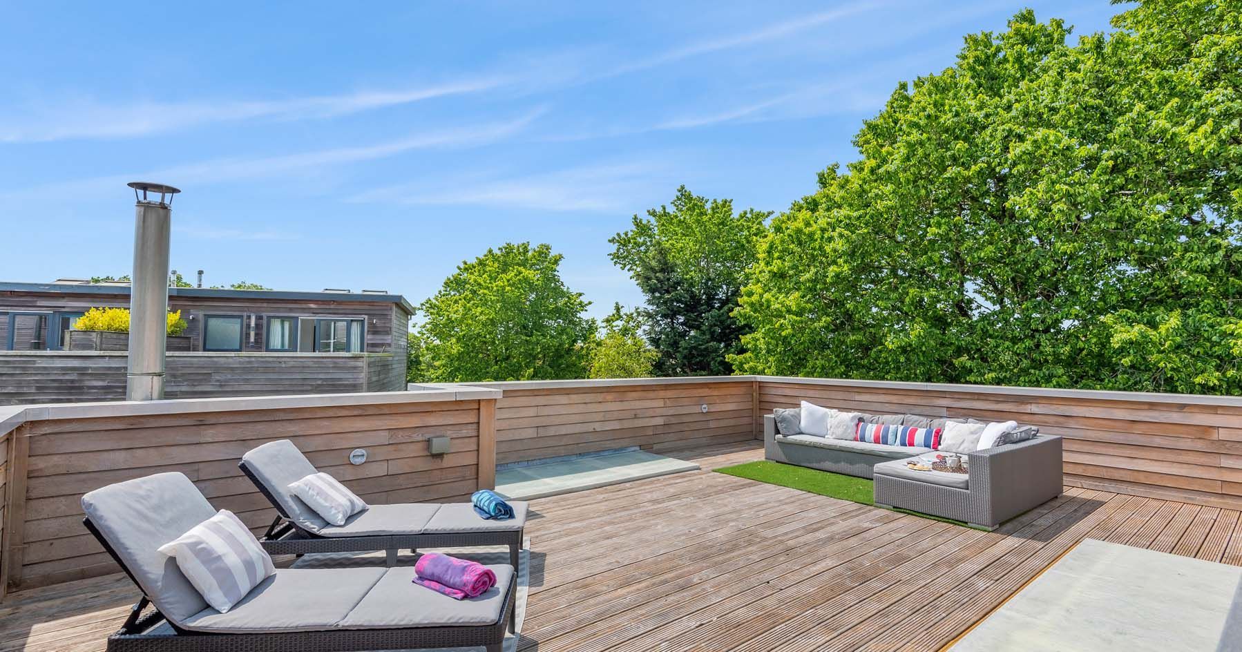 Rooftop deck with lounge chairs and a sofa, surrounded by trees and a blue sky