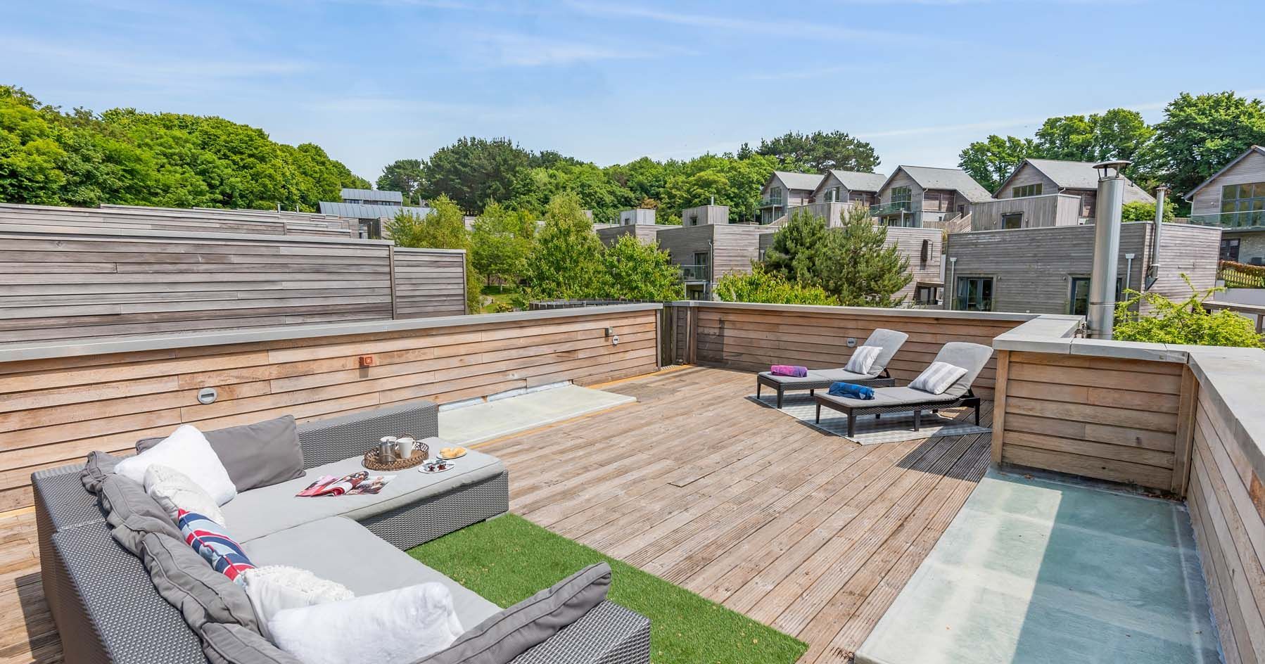 Modern rooftop terrace with outdoor seating and sun loungers surrounded by wooden fences