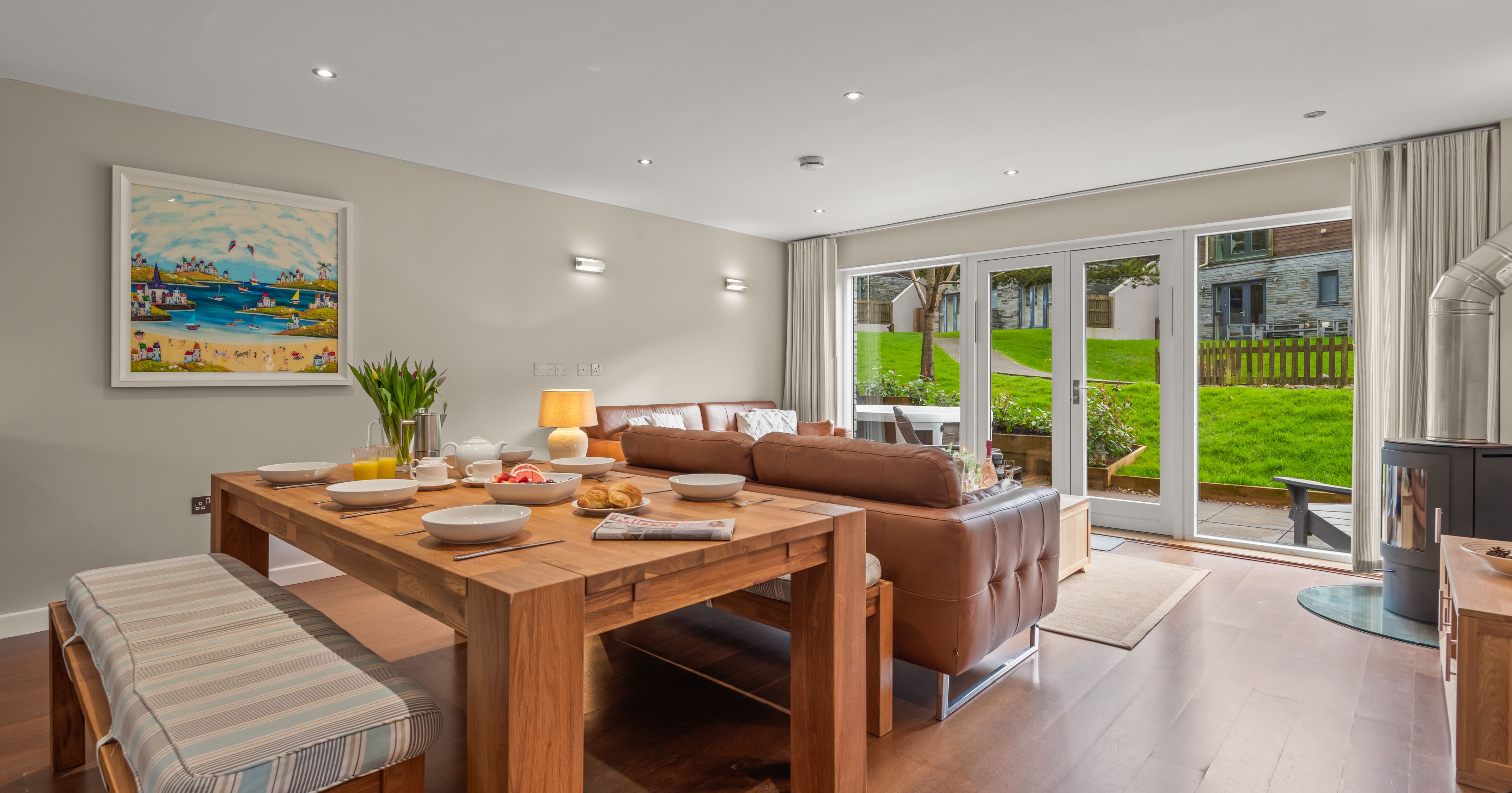 Modern open plan living and dining room with wooden furniture and large glass doors leading to a patio.